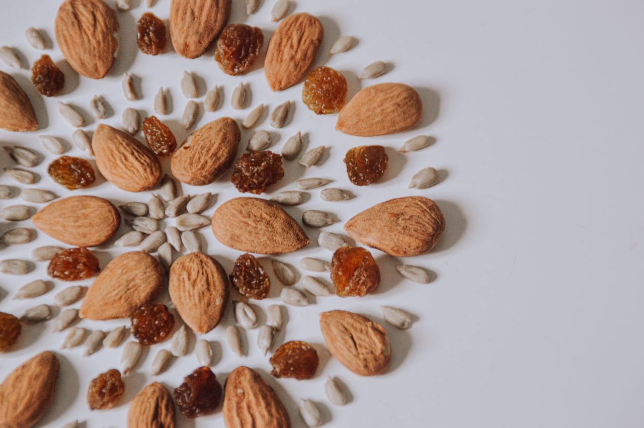 hero-img-01 Artistic pattern of almonds, raisins, and seeds on white surface.