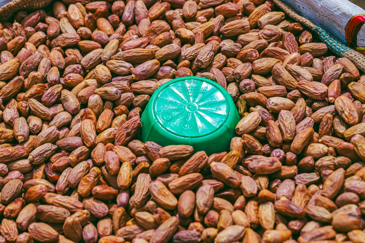 gallery-2 Close-up image of dry date palm fruits with a green plastic bowl in a market setting.