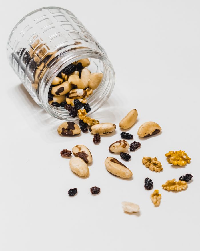services-img A glass jar spills assorted nuts and raisins on a white surface, perfect for snack themes.