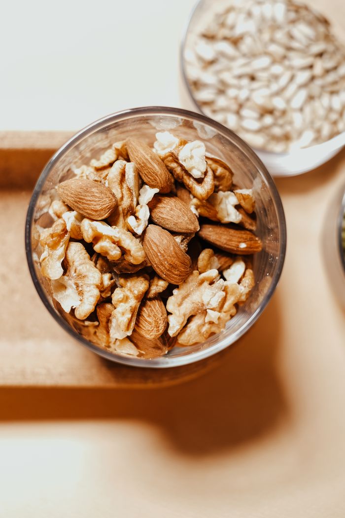 gallery-6 A high-angle shot of almonds and walnuts in a glass bowl on a wooden tray.