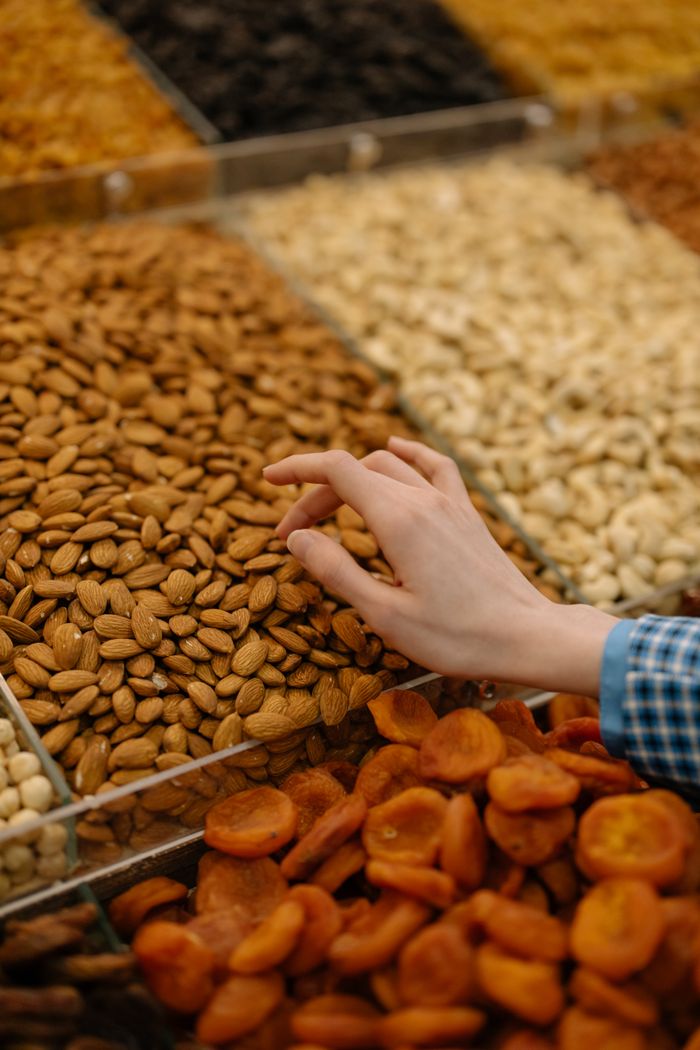 services-03 A hand selecting almonds from a diverse display of nuts and dried fruits at a market.